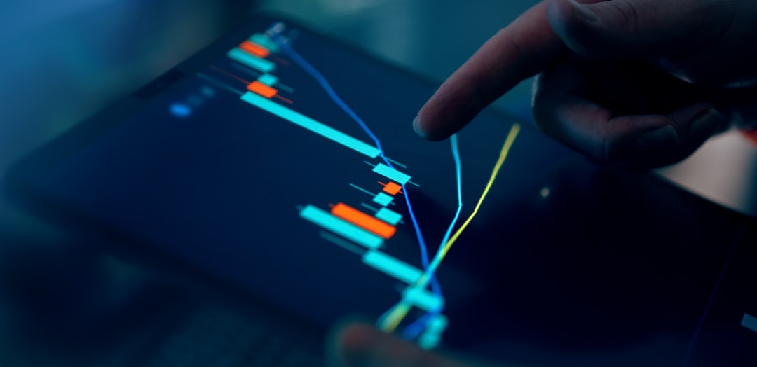 A finger pointing at a digital trading chart on a tablet screen with colorful candlestick graphs