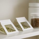 Two white boxes displaying insect traps on a shelf, with jars of brown seeds nearby.